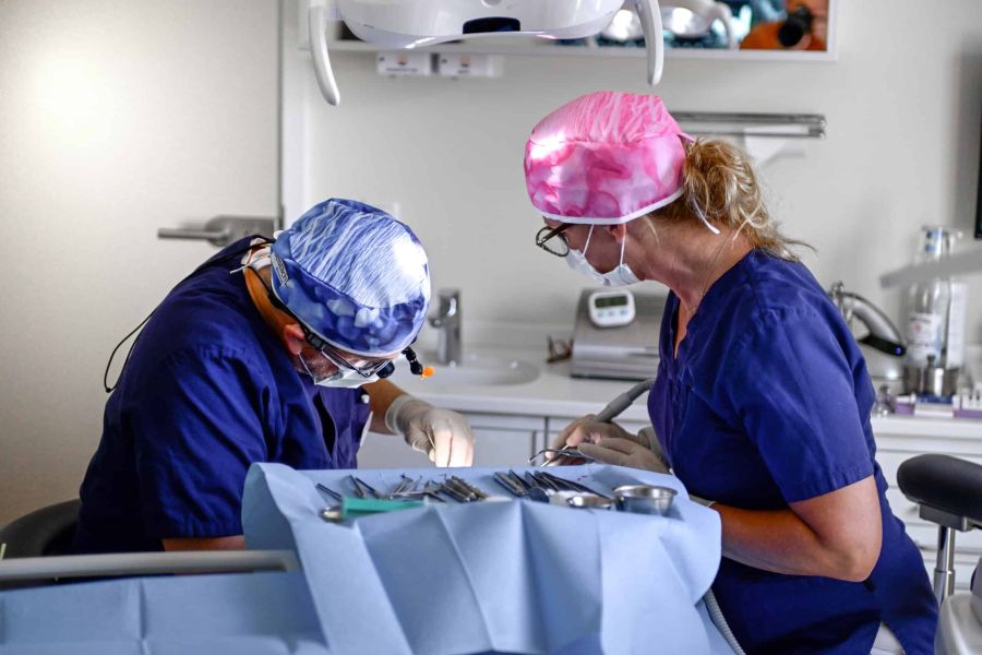 Zwei Zahnmediziner in OP-Kleidung führen eine zahnchirurgische Behandlung durch. Ein steriler OP-Tisch mit Instrumenten ist im Vordergrund.