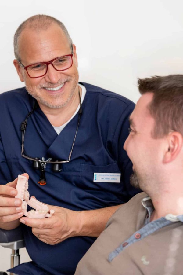 Dr. Dirk Lindner erklärt einem Patienten mit einem Zahnmodell die geplante Behandlung.